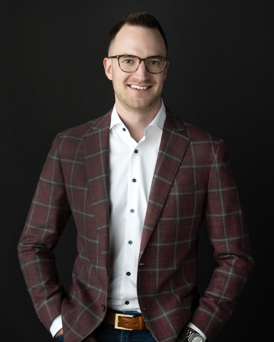 James Green, founder of Dominion AI, leaning against a desk in a dark check jacket, looking toward the camera