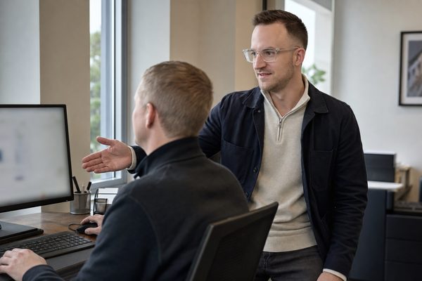 An adviser talking through a workflow with a colleague at their desk, the colleague working the keyboard